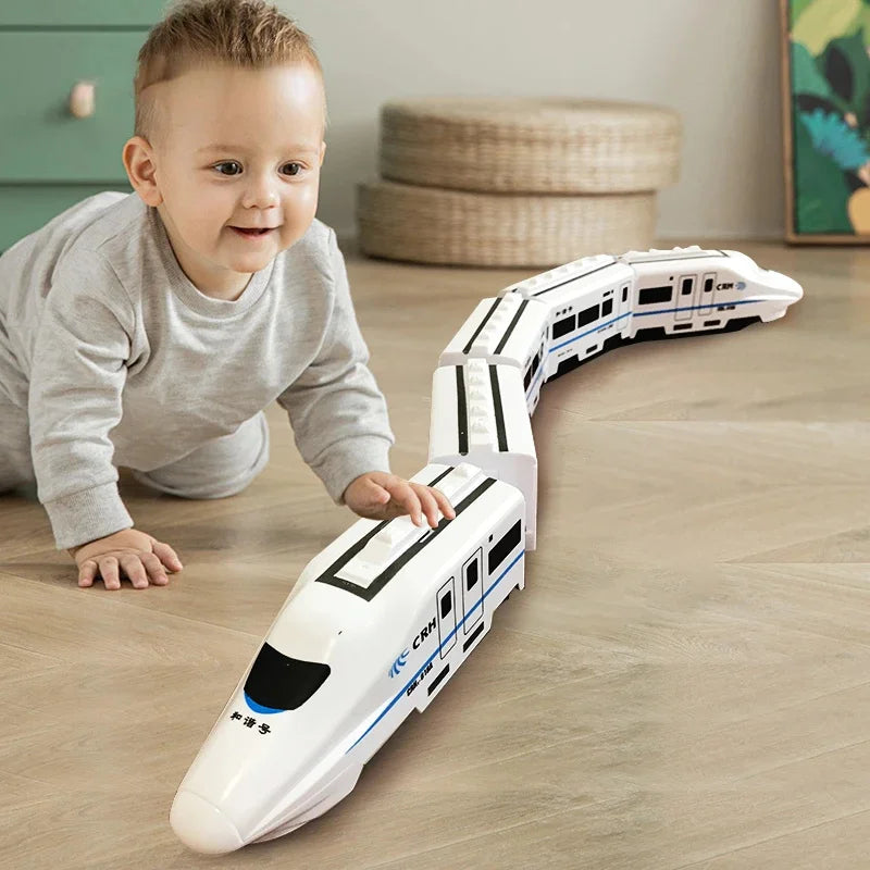 A young child playing with a white electric toy train set on a wooden floor.
