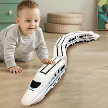 A young child playing with a white electric toy train set on a wooden floor.