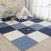 Interlocking foam baby play mat in blue, white, and navy colors, laid out on the floor with children's toys and a play tent in the background.